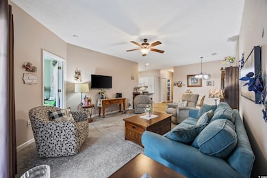 Carpeted living room with a chandelier, ceiling fan, and baseboards