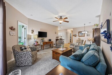 Carpeted living room with a chandelier, ceiling fan, and baseboards