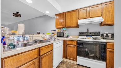 Kitchen featuring white appliances, exhaust hood, light countertops, a sink, and stone finish flooring