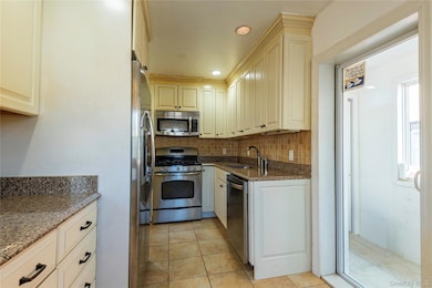 Kitchen featuring dark stone counters, stainless steel appliances, backsplash, cream cabinetry, and light tile patterned floors