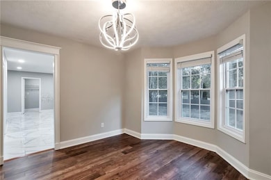 Unfurnished dining area with dark wood-type flooring, a textured ceiling, and a chandelier