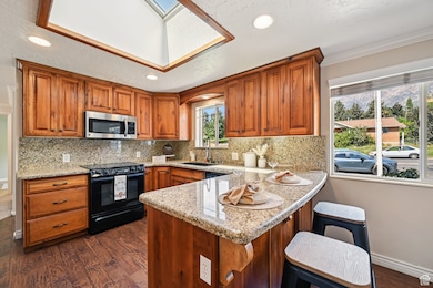 Kitchen featuring dark wood finished floors, brown cabinetry, a peninsula, light stone countertops, and recessed lighting