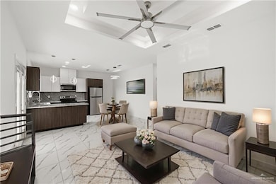 Living area featuring light marble finish flooring, recessed lighting, a tray ceiling, and a ceiling fan