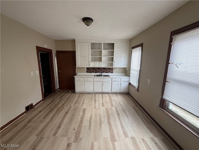 Kitchen with light countertops, light wood-style floors, white cabinets, backsplash, and open shelves