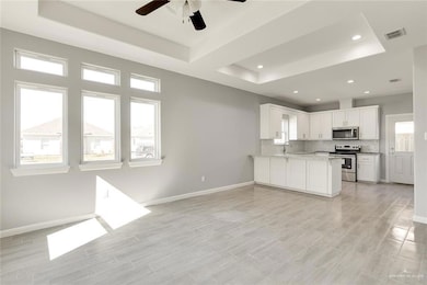 Kitchen with a tray ceiling, appliances with stainless steel finishes, white cabinetry, tasteful backsplash, and a peninsula