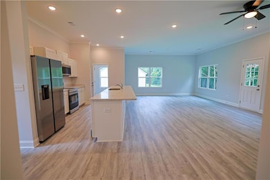 Kitchen with stainless steel appliances, a sink, ornamental molding, white cabinets, and light wood finished floors