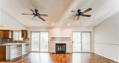 Unfurnished living room featuring a textured ceiling, lofted ceiling, dark wood-style flooring, plenty of natural light, and a fireplace with flush hearth
