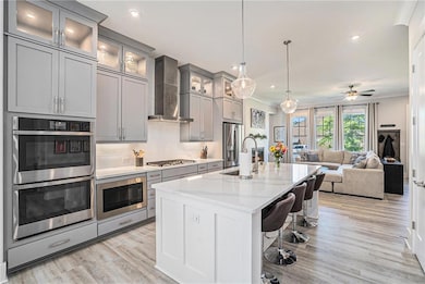 Kitchen featuring stainless steel appliances, wall chimney range hood, gray cabinetry, crown molding, and a sink