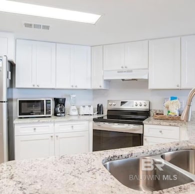 Kitchen with appliances with stainless steel finishes, white cabinets, and light stone counters