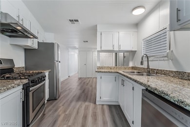 Kitchen featuring ventilation hood, a sink, appliances with stainless steel finishes, visible vents, and white cabinets