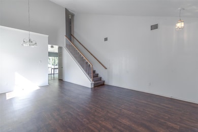 Unfurnished living room with a chandelier, high vaulted ceiling, dark wood-style floors, and stairway