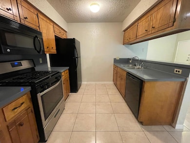 Kitchen featuring black appliances, brown cabinetry, dark countertops, a textured ceiling, and light tile patterned flooring