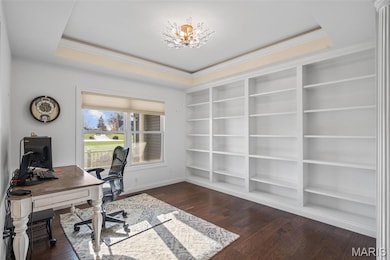 Office space featuring built in features, a tray ceiling, dark wood-style floors, and ornamental molding