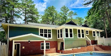 Back of property featuring stairs, an outdoor pool, brick siding, and a patio