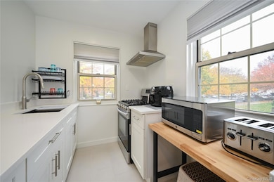 Kitchen with appliances with stainless steel finishes, extractor fan, white cabinetry, and light stone countertops