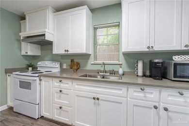 Kitchen with electric range, white cabinets, light stone counters, hardwood / wood-style flooring, and sink