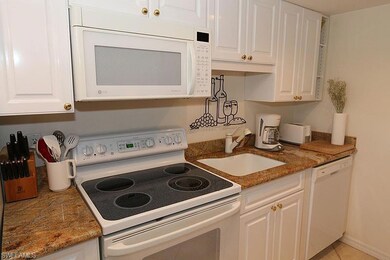Kitchen featuring white appliances, white cabinetry, light tile patterned flooring, and dark stone countertops