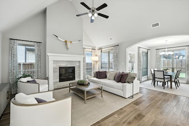 Living area with high vaulted ceiling, wood finished floors, arched walkways, a chandelier, and a tiled fireplace
