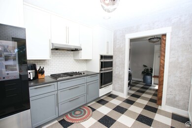 Kitchen featuring dark countertops, gray cabinetry, appliances with stainless steel finishes, decorative backsplash, and white cabinets