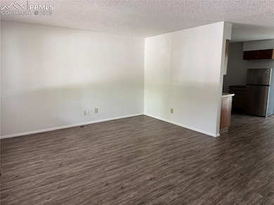 Empty room featuring dark wood finished floors, a textured ceiling, and baseboards