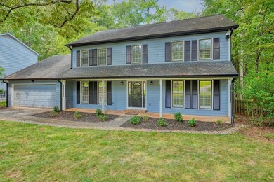 Traditional-style house with a porch, a front lawn, an attached garage, driveway, and roof with shingles