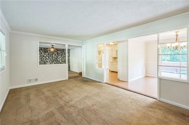 Spare room with light carpet, ornamental molding, baseboards, a chandelier, and a ceiling fan