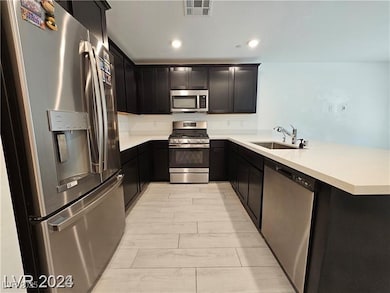 Kitchen featuring appliances with stainless steel finishes, a peninsula, recessed lighting, dark cabinets, and light stone countertops