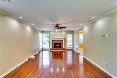 Unfurnished living room featuring ceiling fan, crown molding, wood finished floors, a brick fireplace, and recessed lighting