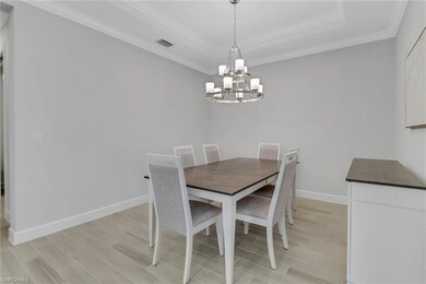 Dining area with a notable chandelier, light wood-style flooring, crown molding, visible vents, and a raised ceiling