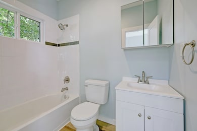 Full bathroom is light and bright with white shower tile, vanity with quartz counter, and mirrored medicine cabinet.
