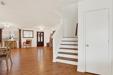 This photo showcases a spacious, open-concept living area with light wood flooring, a staircase, and a cozy dining setup by large windows.