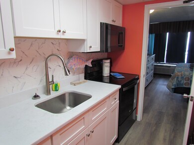 Kitchen with black appliances, a sink, white cabinetry, decorative backsplash, and wood finished floors