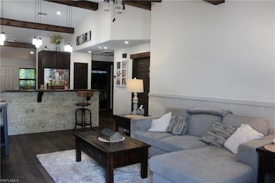Living area featuring beam ceiling, dark wood-style floors, high vaulted ceiling, and a wainscoted wall