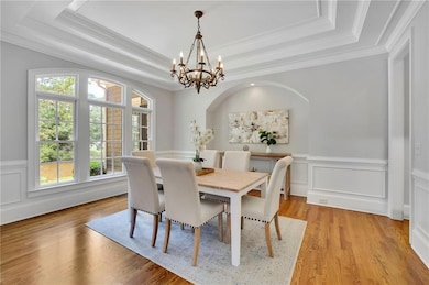 Dining area featuring a raised ceiling, a chandelier, crown molding, wainscoting, and light wood finished floors