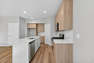 Kitchen with light stone countertops, modern cabinets, tasteful backsplash, stainless steel appliances, and light brown cabinetry