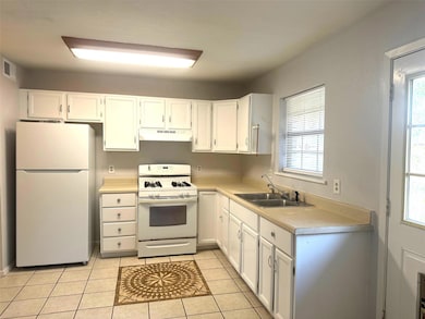 Kitchen with white appliances, white cabinetry, light countertops, and light tile patterned flooring