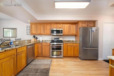 Kitchen featuring appliances with stainless steel finishes, light stone counters, a sink, and brown cabinetry