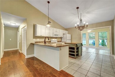 Kitchen featuring white appliances, white cabinetry, hanging light fixtures, a peninsula, and vaulted ceiling
