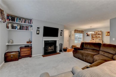 Living room featuring a chandelier, carpet flooring, a fireplace, baseboards, and a textured ceiling
