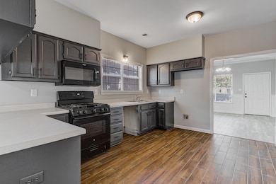 Kitchen with black appliances, dark wood-style floors, light countertops, and a chandelier