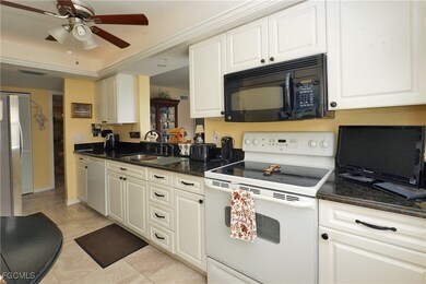 Kitchen featuring white appliances, white cabinets, light tile patterned floors, dark stone counters, and a ceiling fan