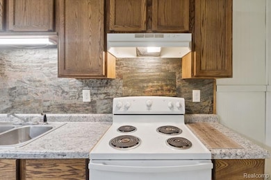Kitchen with electric range, under cabinet range hood, light countertops, backsplash, and brown cabinetry