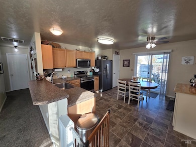 Kitchen with appliances with stainless steel finishes, a textured ceiling, a ceiling fan, a breakfast bar area, and dark countertops