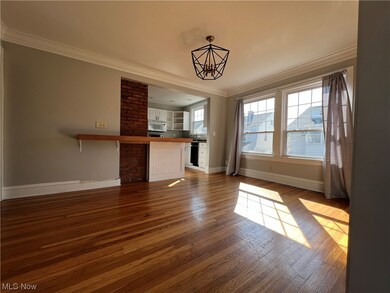 Unfurnished living room with brick wall, crown molding, and hardwood / wood-style flooring