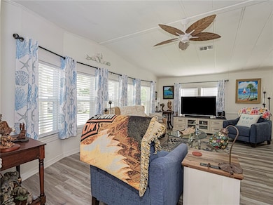 Living area with plenty of natural light, wood finished floors, vaulted ceiling, and a ceiling fan