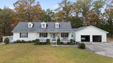 Cape cod-style house featuring covered porch, a shingled roof, concrete driveway, an attached garage, and a front yard