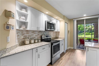 Kitchen with stainless steel appliances, white cabinets, open shelves, tasteful backsplash, and recessed lighting