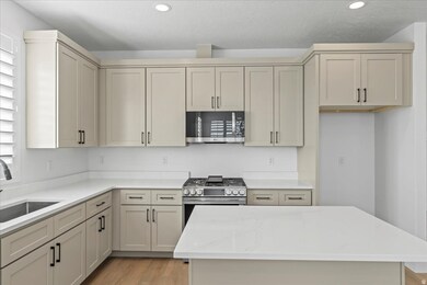 Kitchen featuring light stone countertops, cream cabinets, stainless steel microwave, light wood-style floors, and a kitchen island