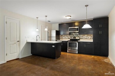 Kitchen featuring appliances with stainless steel finishes, a peninsula, decorative backsplash, light countertops, and finished concrete flooring
