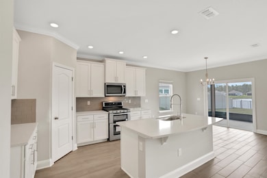 Kitchen with crown molding, appliances with stainless steel finishes, tasteful backsplash, a center island with sink, and white cabinets